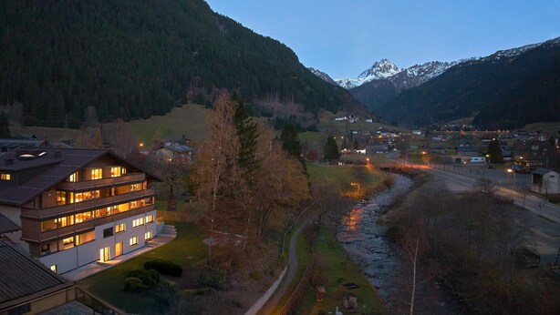 A multi-story hotel with balconies, a river, and mountains in the background. - Suite with private sauna (Gaschurn)
