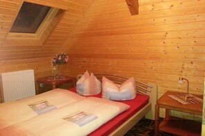 Ein Zimmer in einer Holzhütte mit einem Bett, einem kleinen Tisch, einem Nachttisch und einem Fenster.