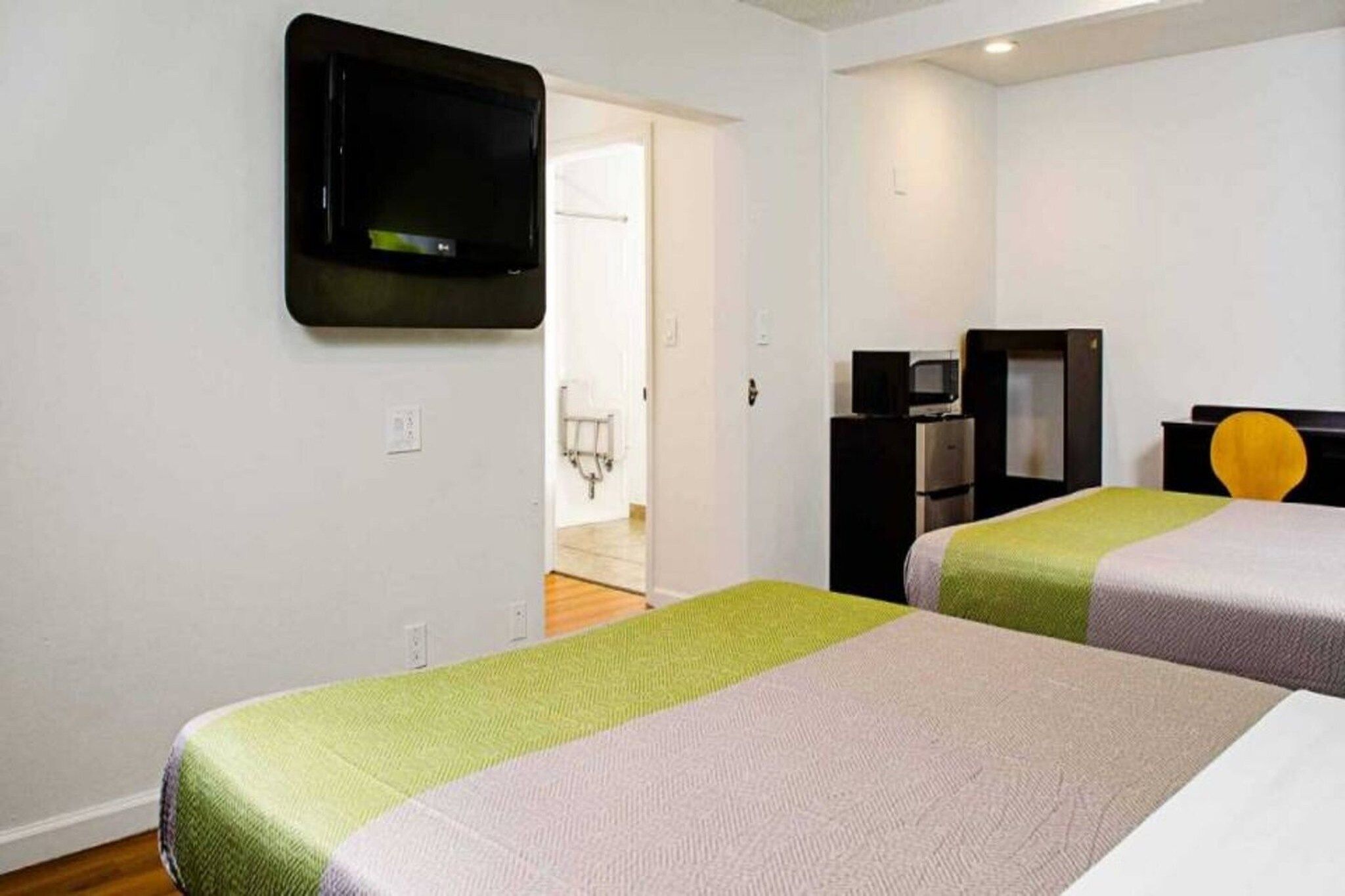 Ein Hotelzimmer mit zwei Betten, einem an der Wand befestigten Fernseher, einer Mikrowelle und einem kleinen Schreibtisch mit Stuhl.