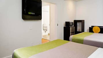 Ein Hotelzimmer mit zwei Betten, einem an der Wand befestigten Fernseher, einer Mikrowelle und einem kleinen Schreibtisch mit Stuhl.