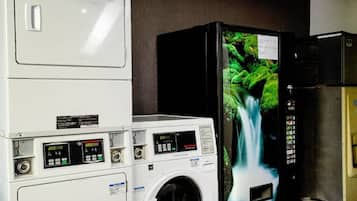 A laundry facility with stacked dryers and a washing machine, a vending machine with a waterfall image, and a refrigerator.