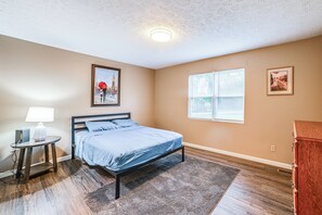 A bedroom with a bed, a bedside table with a lamp, a window with blinds, and two framed pictures on the wall. - Gateway to Kentucky Lake! Retreat 1 Mi to Main St (Waverly)