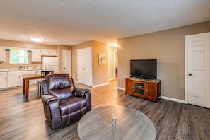 A living room with a leather chair, a round coffee table, a television on a wooden stand, and a kitchen in the background. - Gateway to Kentucky Lake! Retreat 1 Mi to Main St (Waverly)