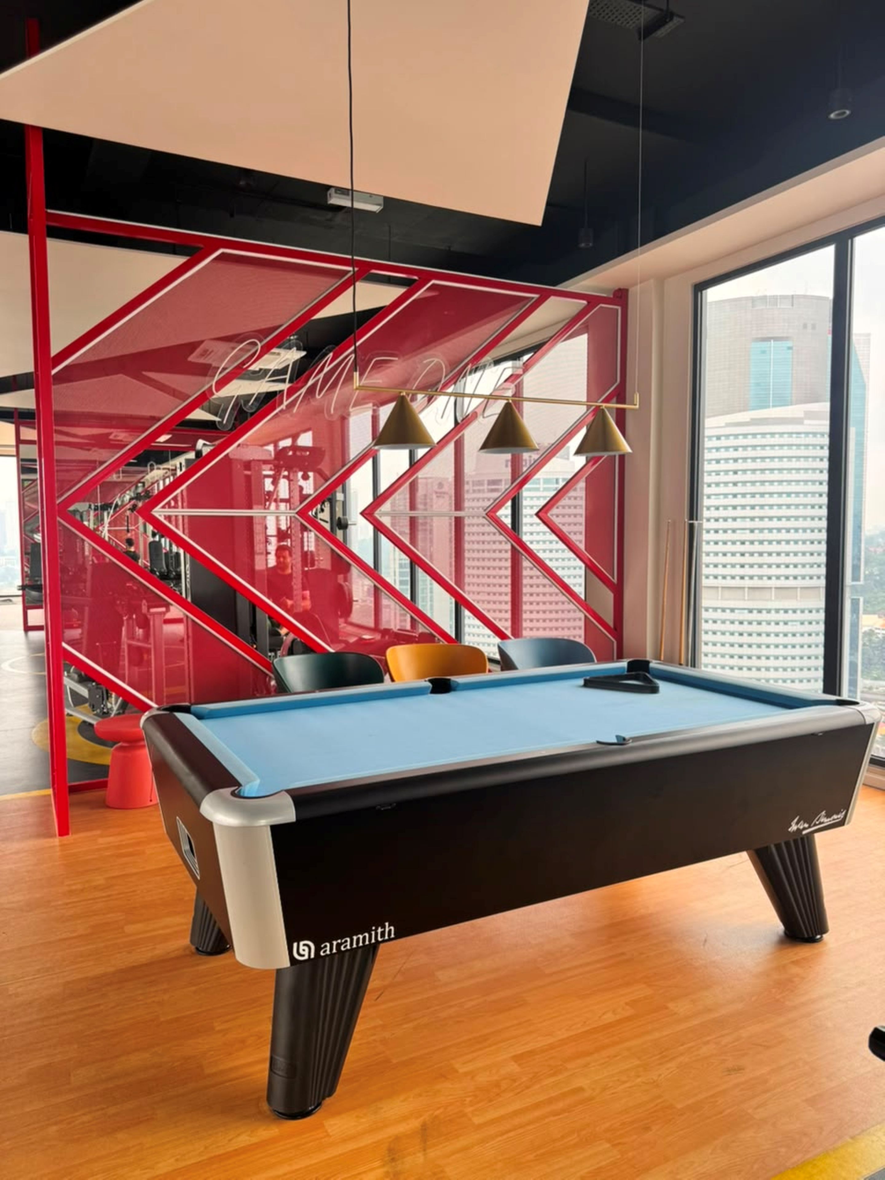 Una mesa de billar de diseño moderno, un separador geométrico rojo y vistas de la ciudad a través de grandes ventanales.