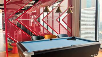 Una mesa de billar de diseño moderno, un separador geométrico rojo y vistas de la ciudad a través de grandes ventanales.