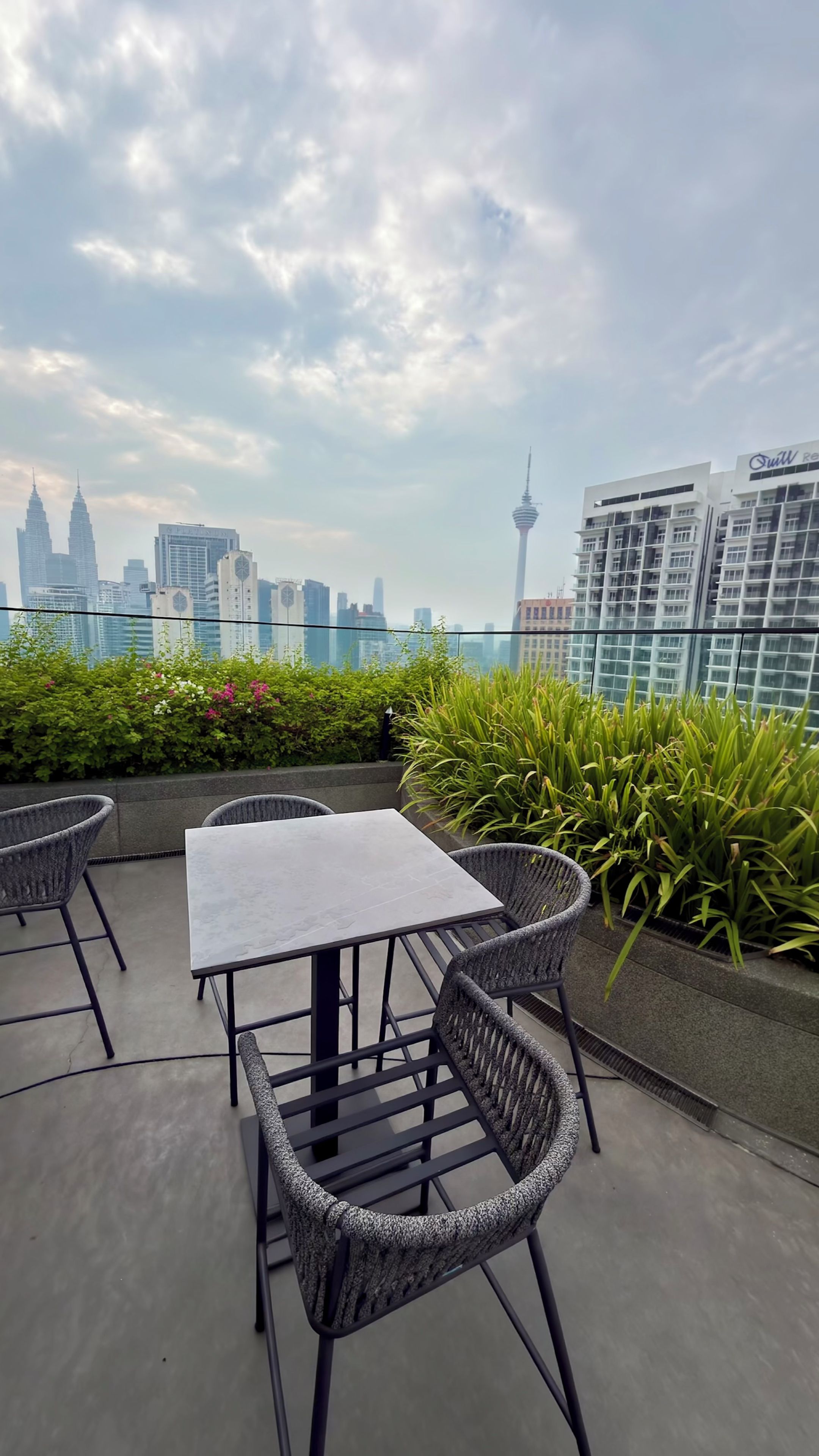Un espace extérieur aménagé avec une table et des chaises, entouré de verdure, offrant une vue sur les toits d’une ville et ses bâtiments emblématiques.