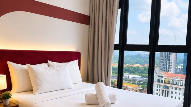 A hotel room with a large bed, a nightstand, a lamp, and a view of the city through large windows. - Majestic Residence KLCC  by Maju Inn (Kuala Lumpur)