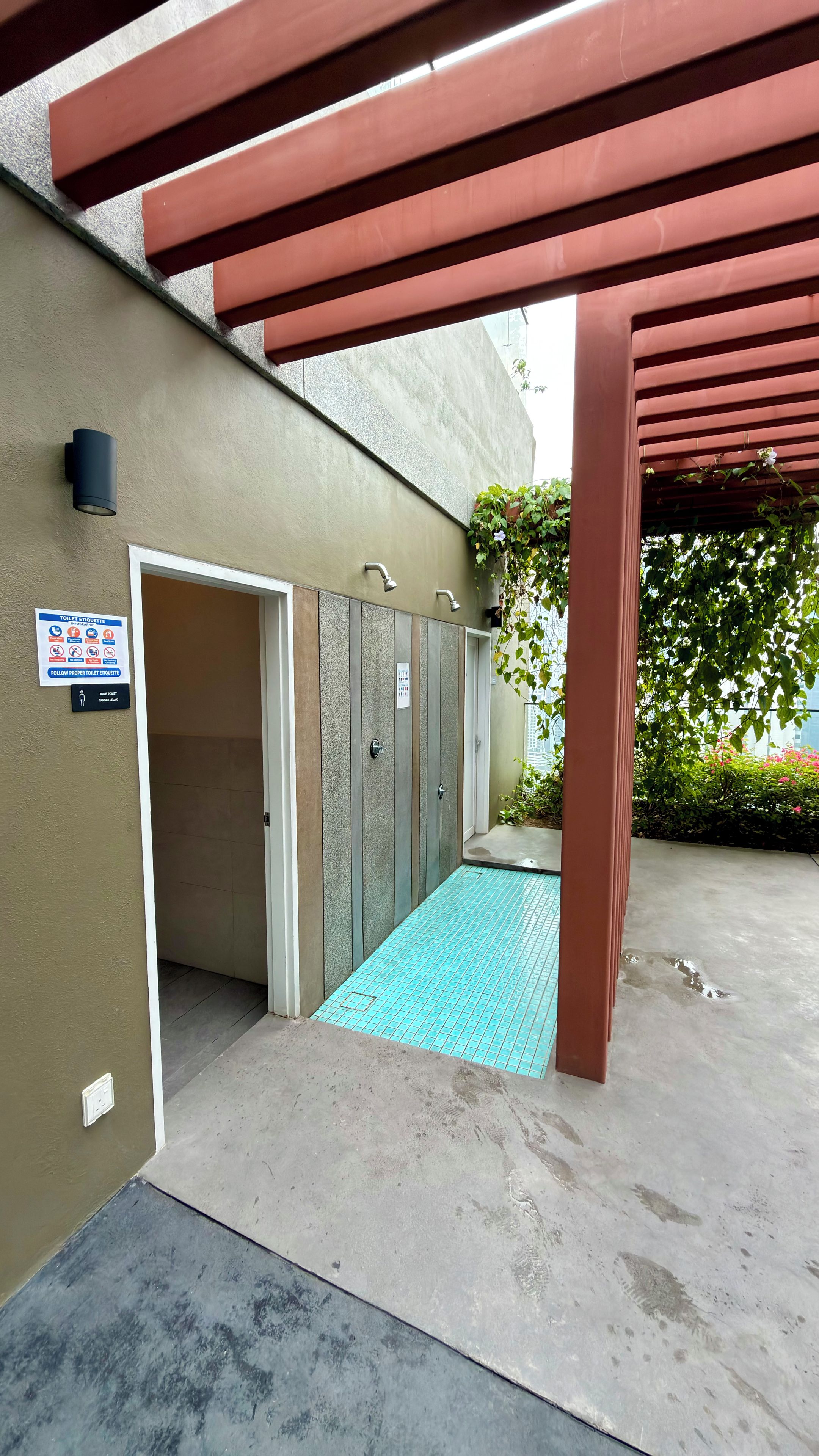 Un espacio al aire libre cubierto con un box de ducha, un cartel con indicaciones sobre el uso del baño y un aplique de luz en la pared.