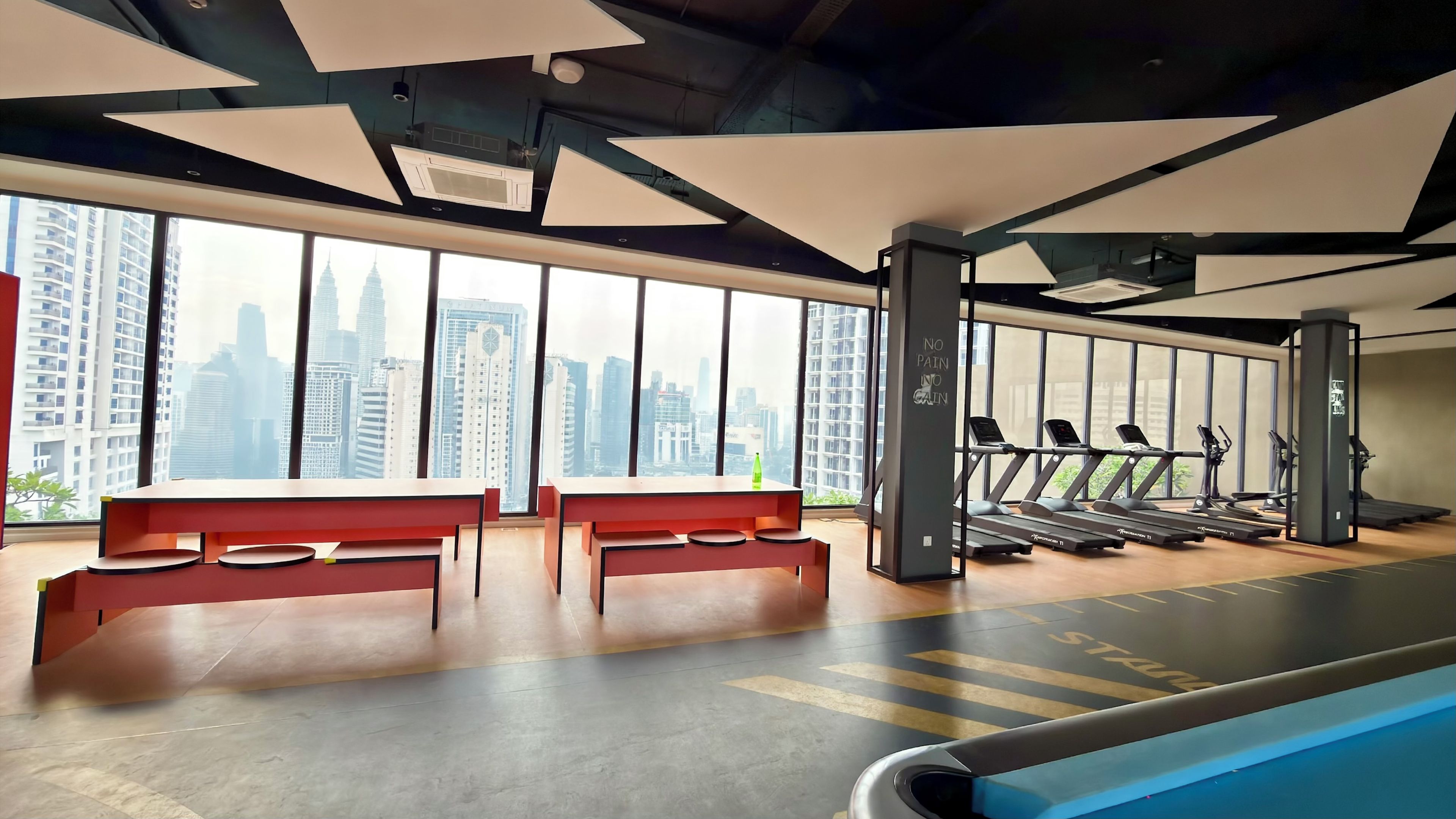 Un gimnasio con equipamiento de ejercicio, bancos y grandes ventanales con vistas a la ciudad.