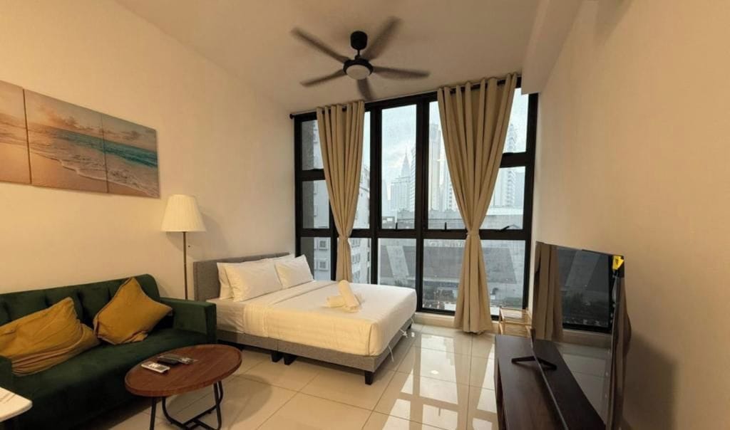 Habitación de hotel con cama, sofá, televisión y ventana con cortinas.