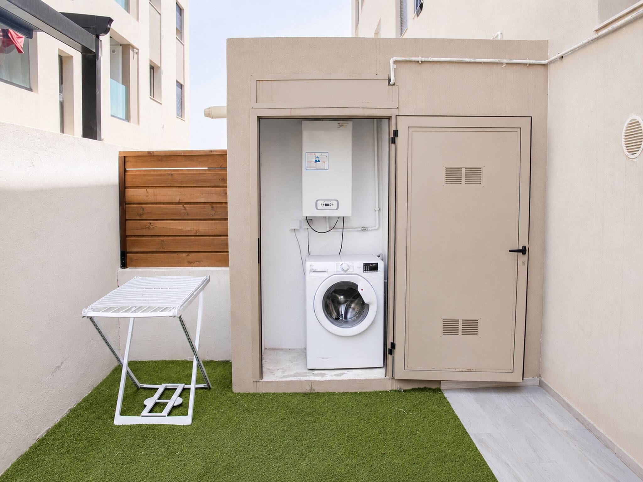 A compact laundry area with a washing machine, a drying rack, and a utility cabinet.