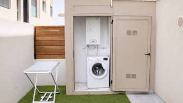 A compact laundry area with a washing machine, a drying rack, and a utility cabinet.