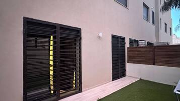A modern building with large black shutters on the windows, a wooden fence, and a small patch of artificial grass.