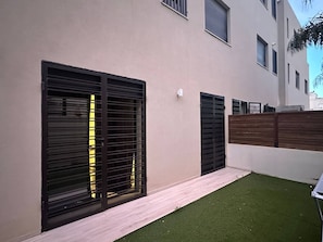 A modern building with large black shutters on the windows, a wooden fence, and a small patch of artificial grass. - Luxury apartment, one bedroom, prestigious residence (Marsa)