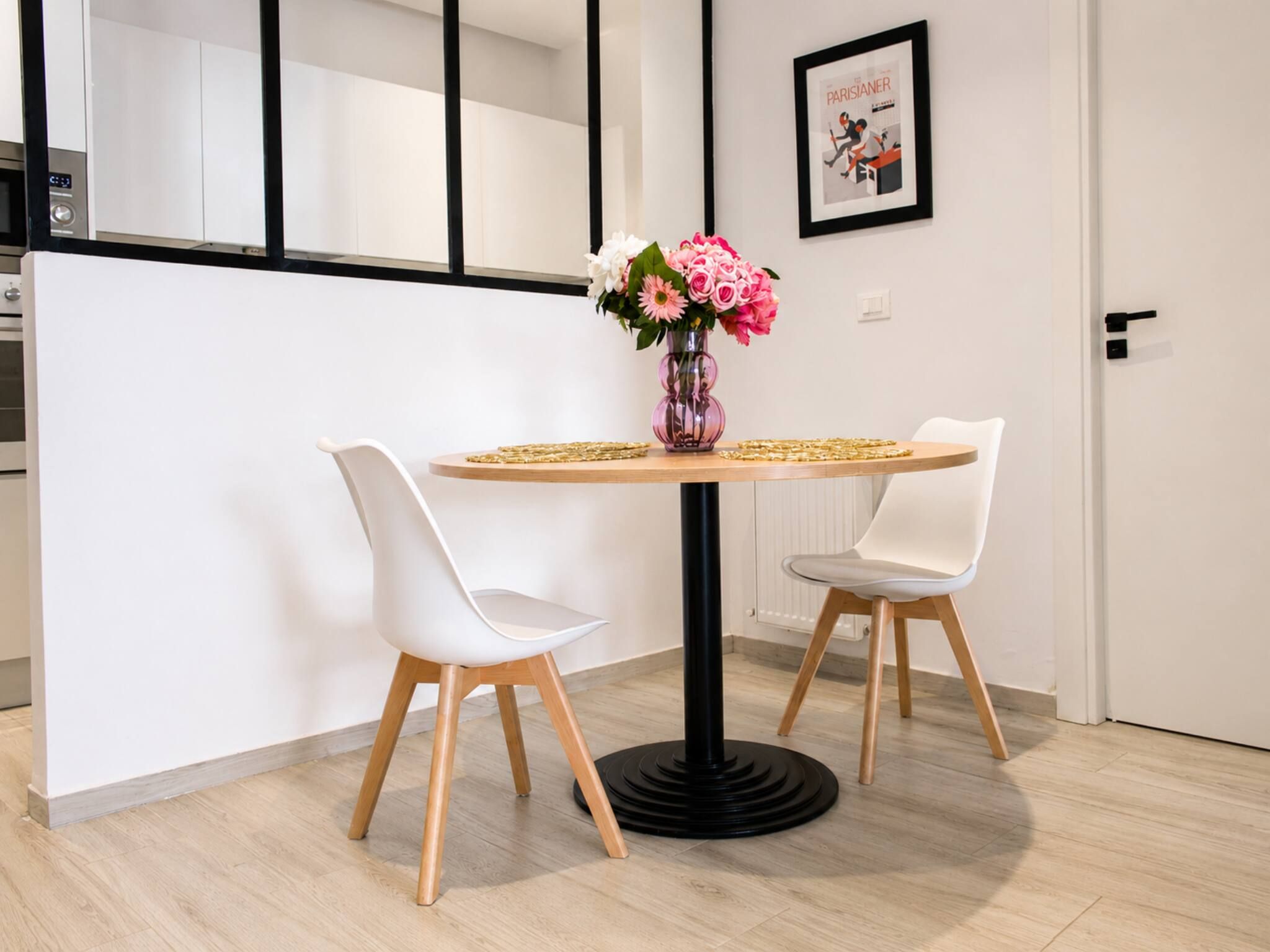 Uma sala de jantar moderna com uma mesa redonda, duas cadeiras brancas e um vaso com flores.