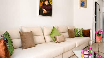 A modern living room with a sofa, cushions, a glass coffee table, and a painting on the wall.