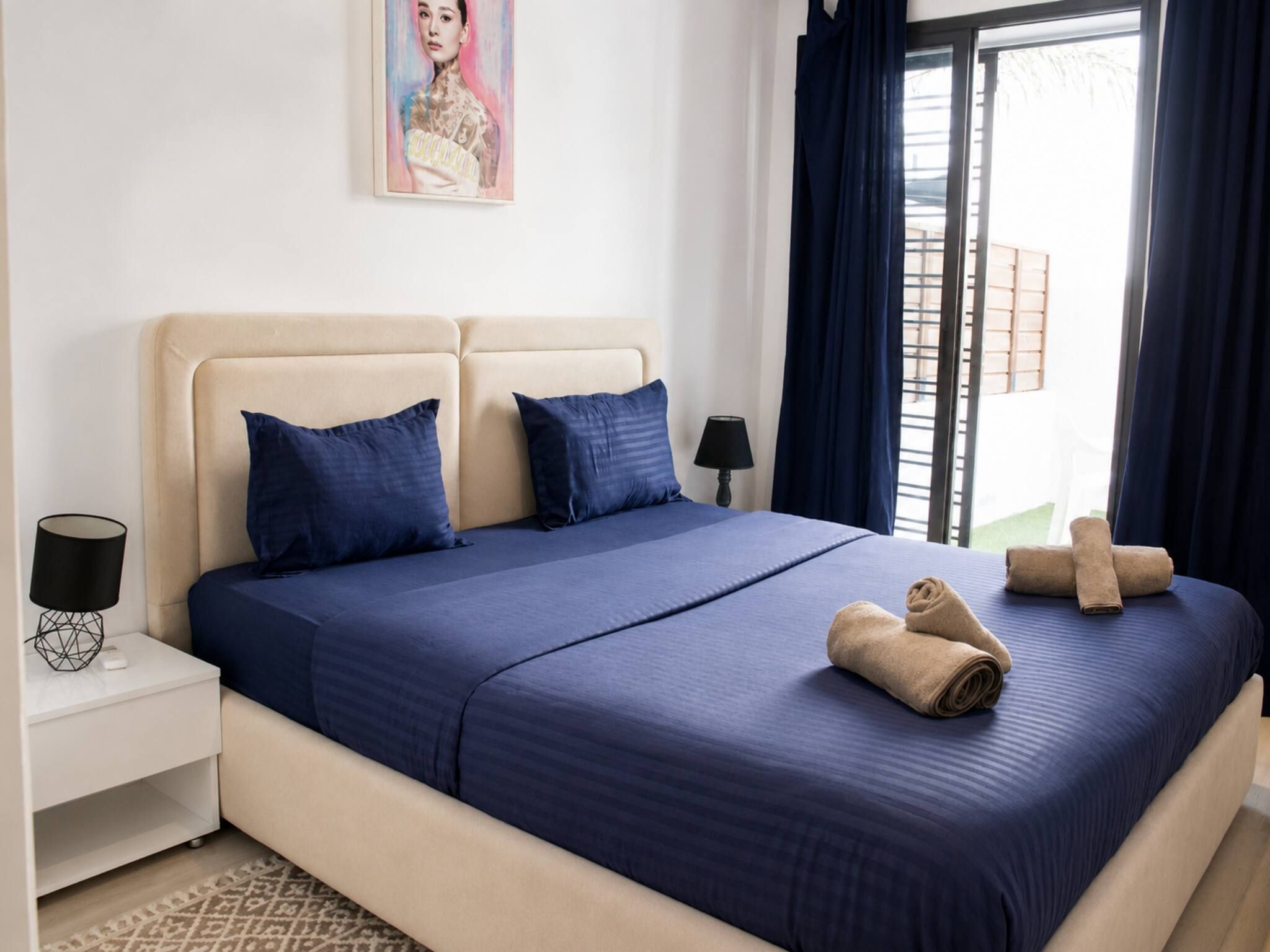 A hotel room with a bed, two pillows, a nightstand with a lamp, and a window with curtains.