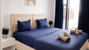 A hotel room with a bed, two pillows, a nightstand with a lamp, and a window with curtains.