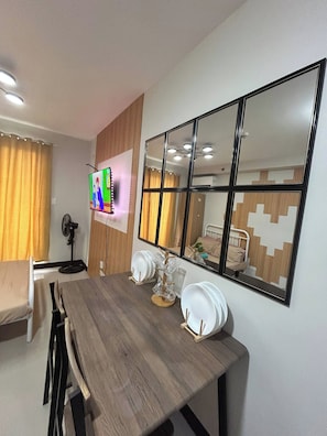 A dining area with a wooden table, chairs, a TV mounted on the wall, and a large mirror reflecting the room. - Pool-view near airport  Saekyung Village Phase 3 (Lapu-Lapu)