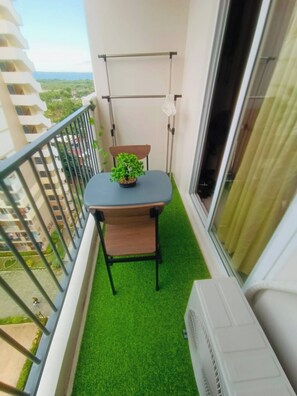 Een balkon met een kleine tafel, een stoel, een bloempot en een raam met gordijnen.