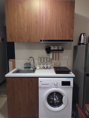 Eine kompakte Küche mit Holzschränken, einer eingebauten Waschmaschine, einem Edelstahl-Wasserkocher und einer Kaffeemaschine.