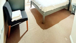 Een slaapkamer met een bed, een stoel, een lamp en een raam met gordijnen.