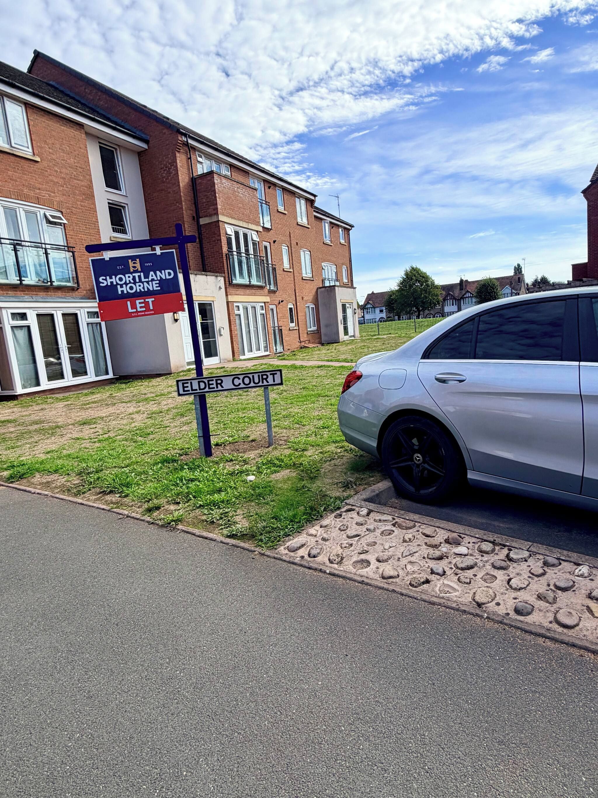 Een woonwijk met een bordje voor Shortland Horne Let, een witte auto geparkeerd aan de straat, en een bord met de straatnaam Elder Court.