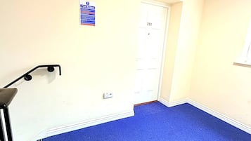 Een kamer met een blauw tapijt, een witte deur met het nummer 251 en een wit plafond met een geperforeerd patroon.