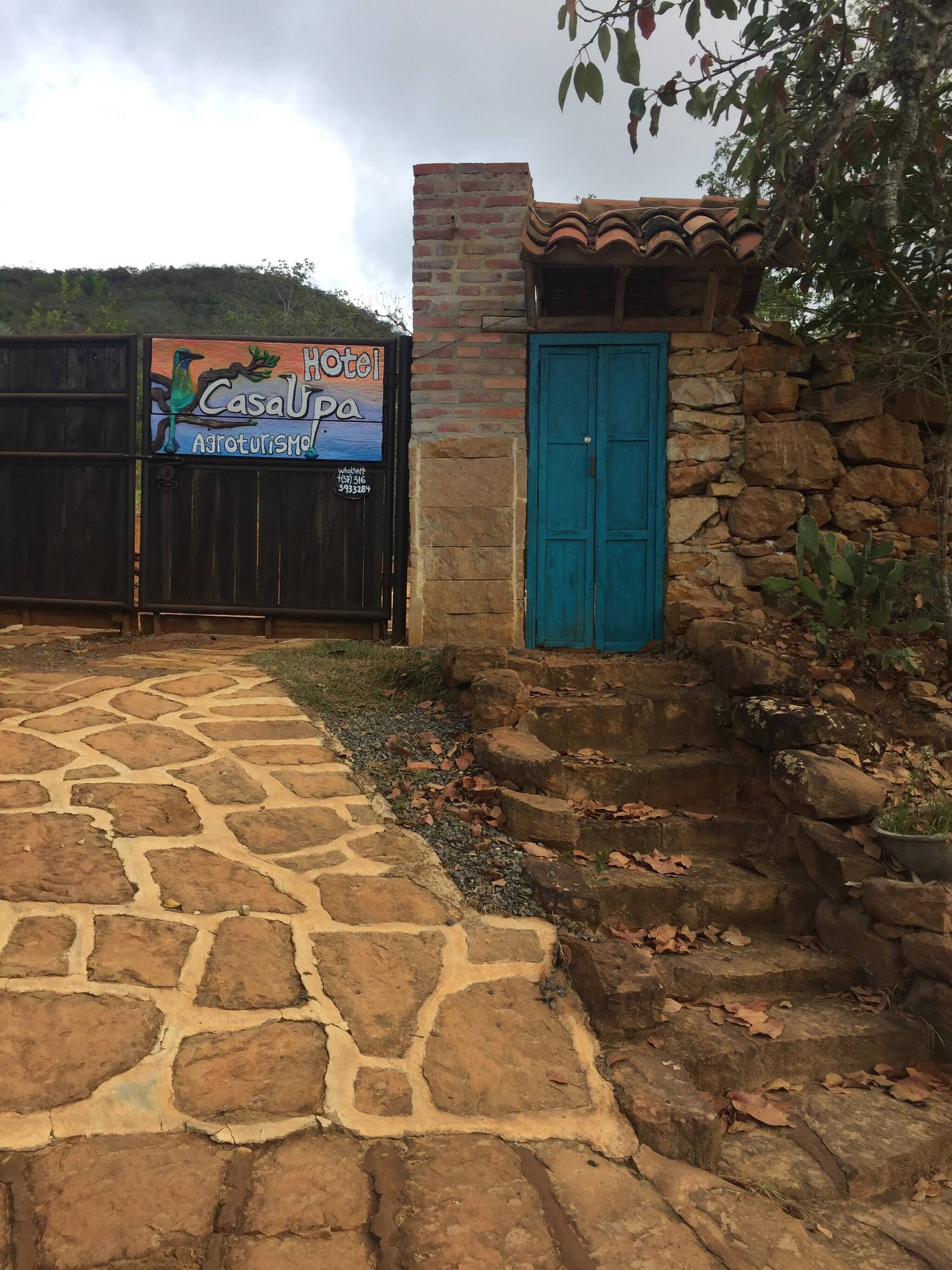 Un sendero de piedra conduce a un edificio con una puerta azul y un letrero que dice 'Hotel Casa de Aroterosimo'.