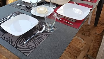 A table set outdoors with plates, glasses, and cutlery, a toaster oven, and a brick wall in the background.