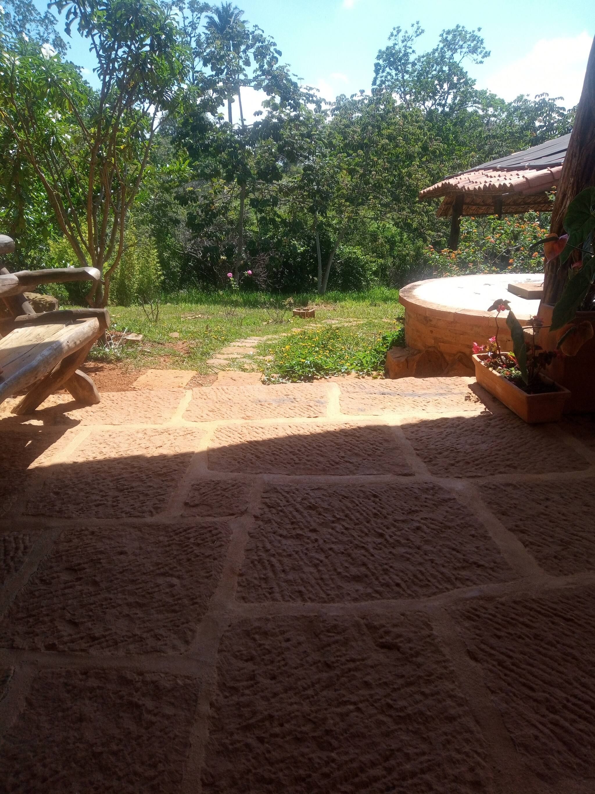 Un patio de piedra con un banco de madera, una estructura circular de piedra y diversas plantas.