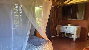 Een kamer met een bed onder een klamboe, een houten kast en een televisietoestel.