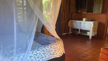 Quarto com cama sob uma mosquiteira, um armário de madeira e uma televisão.
