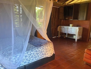Quarto com cama sob uma mosquiteira, um armário de madeira e uma televisão.