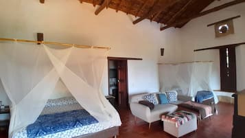 A room with a bed under a mosquito net, a sofa with cushions, and a wooden ceiling.