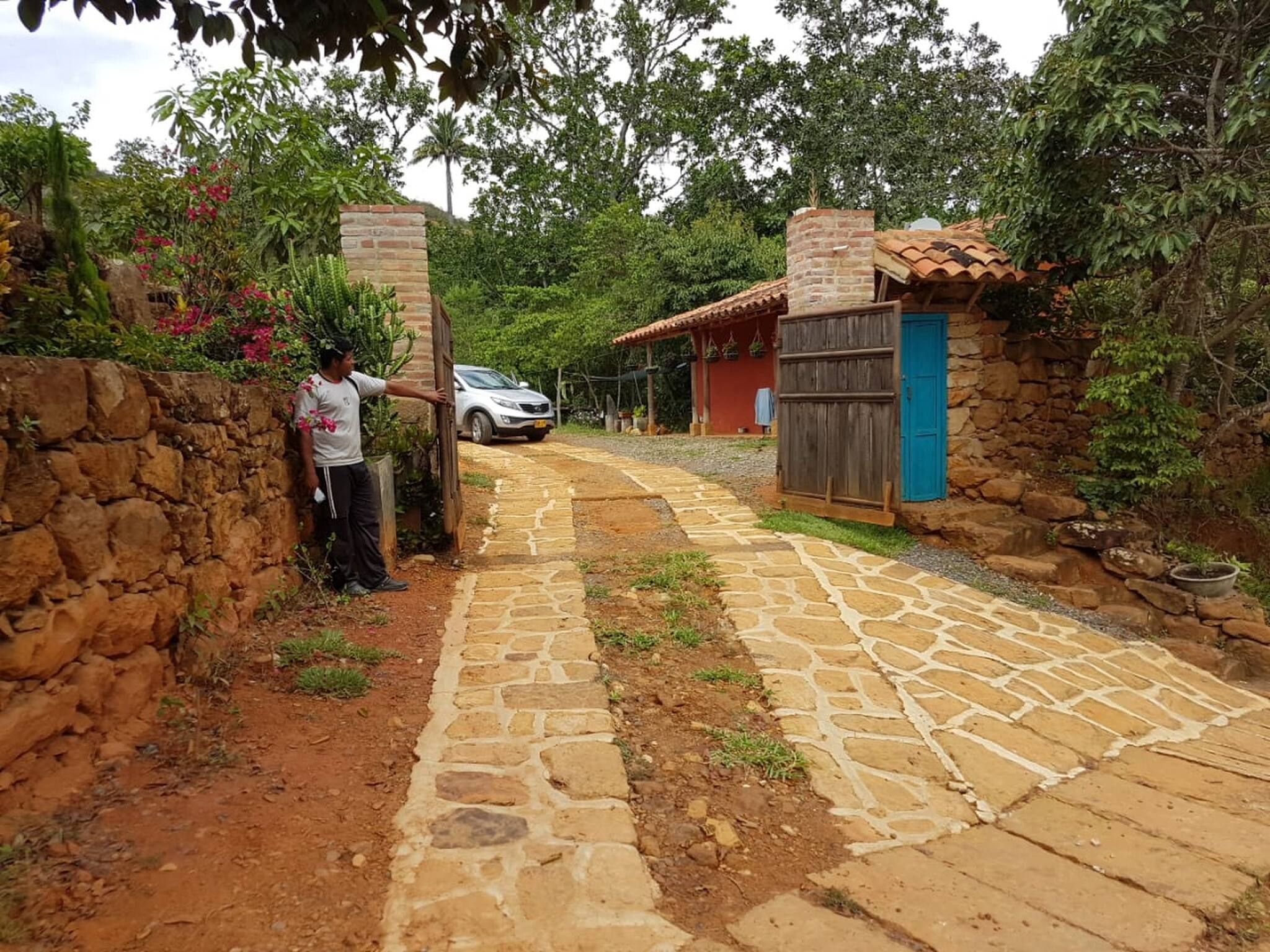 A stone pathway leading to a rustic building with a blue door, surrounded by greenery.