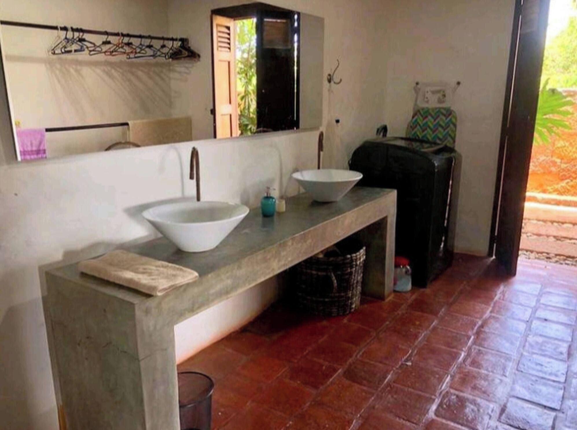 A bathroom with a concrete countertop, two sinks, a mirror, and a towel rack.