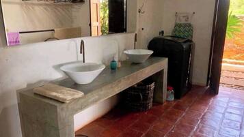 A bathroom with a concrete countertop, two sinks, a mirror, and a towel rack.