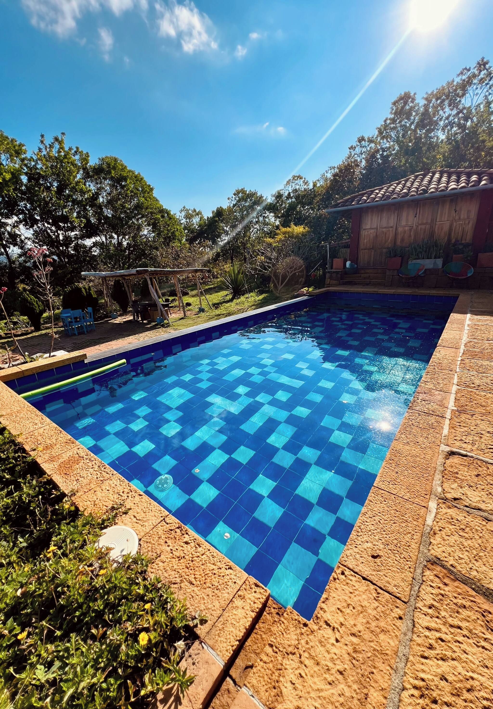 Una piscina con diseño de cuadros, rodeada por una terraza de madera y un jardín.