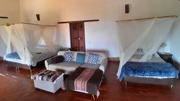 A room with two beds, each with a canopy, a sofa, and a small table.