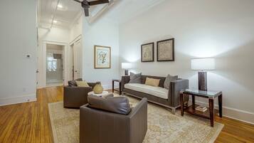 A spacious living room with a sofa, a coffee table, and a lamp. There is a door leading to a bathroom with a shower.