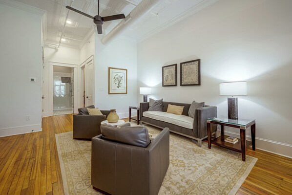 A spacious living room with a sofa, a coffee table, and a lamp. There is a door leading to a bathroom with a shower.