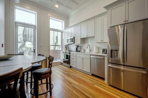 A modern kitchen with stainless steel appliances, white cabinetry, and a wooden floor.