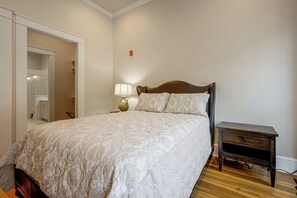 Un dormitorio con cama, mesita de noche, lámpara y puerta que da a un baño.