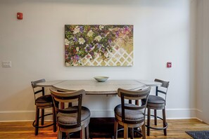 A dining area with a round table, four chairs, and a floral painting on the wall.
