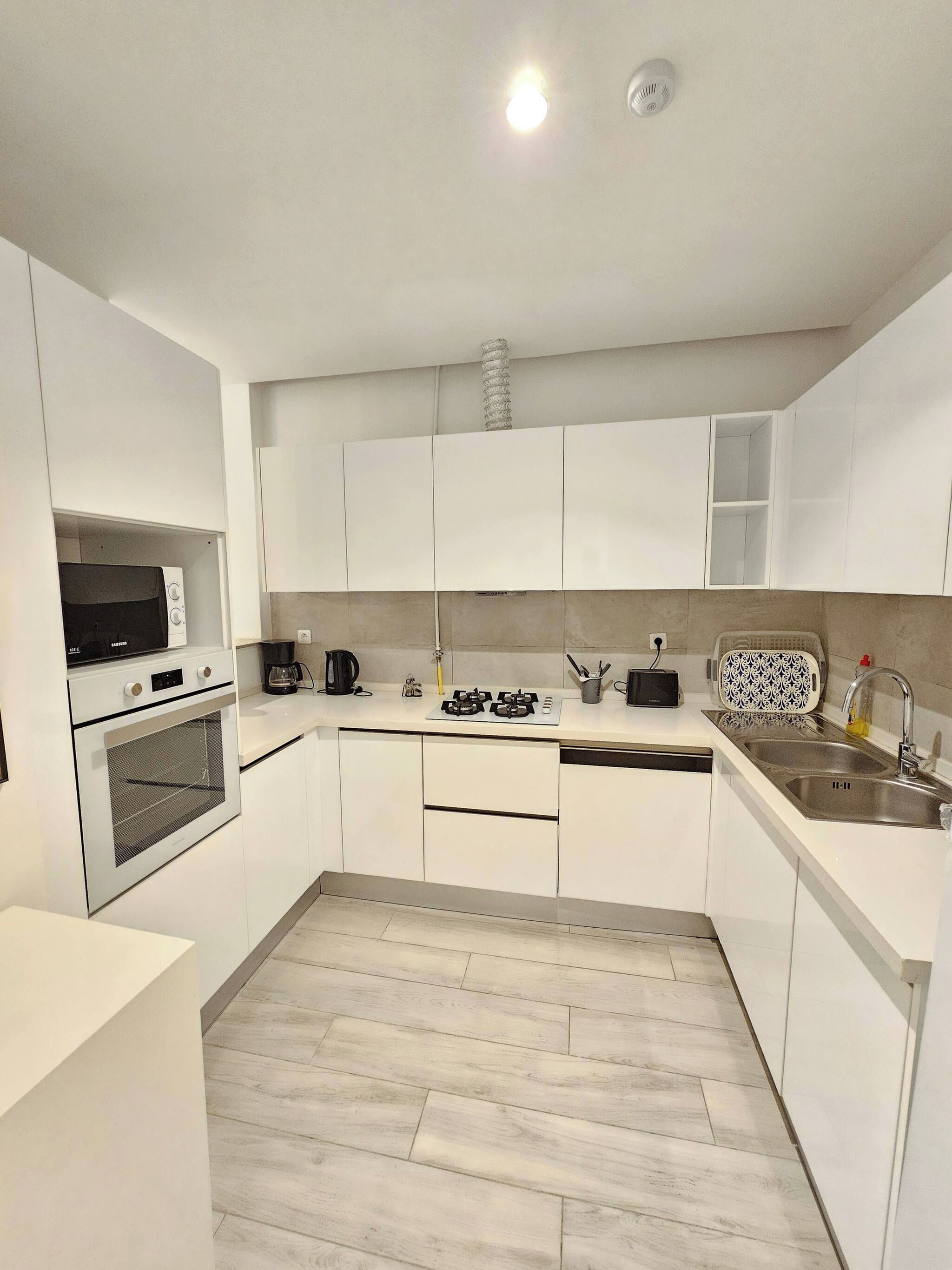 Una cucina moderna con mobili bianchi, forno integrato, microonde, piano cottura a gas e lavello.