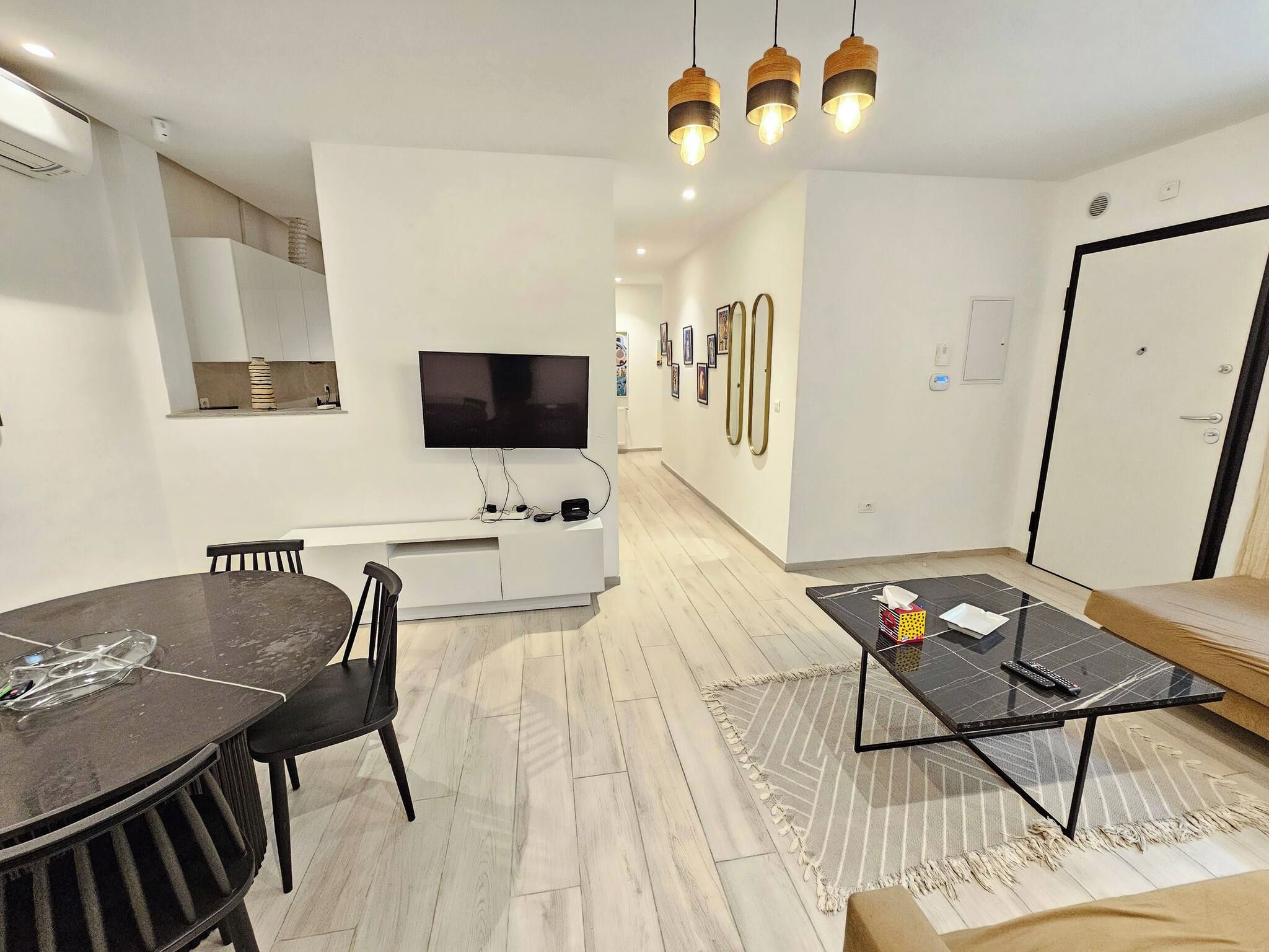 Ein modernes Wohnzimmer mit Essbereich, einer Couch, einem Couchtisch und einem an der Wand befestigten Fernseher.