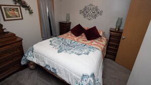Une chambre à coucher comprenant un lit, une commode, une table de chevet, un élément de décoration murale et une porte.