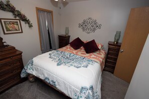 Quarto com cama, penteadeira, mesa de cabeceira, decoração na parede e uma porta.