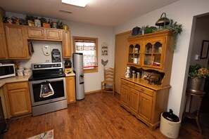 A kitchen with wooden cabinets, a stainless steel stove, a refrigerator, and a window with a curtain.